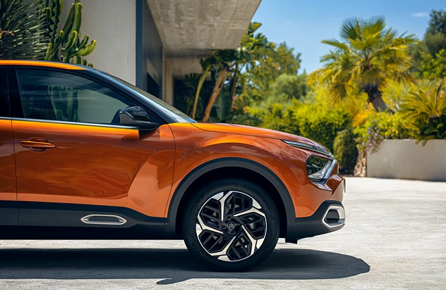 Seitenansicht eines orangefarbenen Citroën vor einem modernen Gebäude mit Palmen