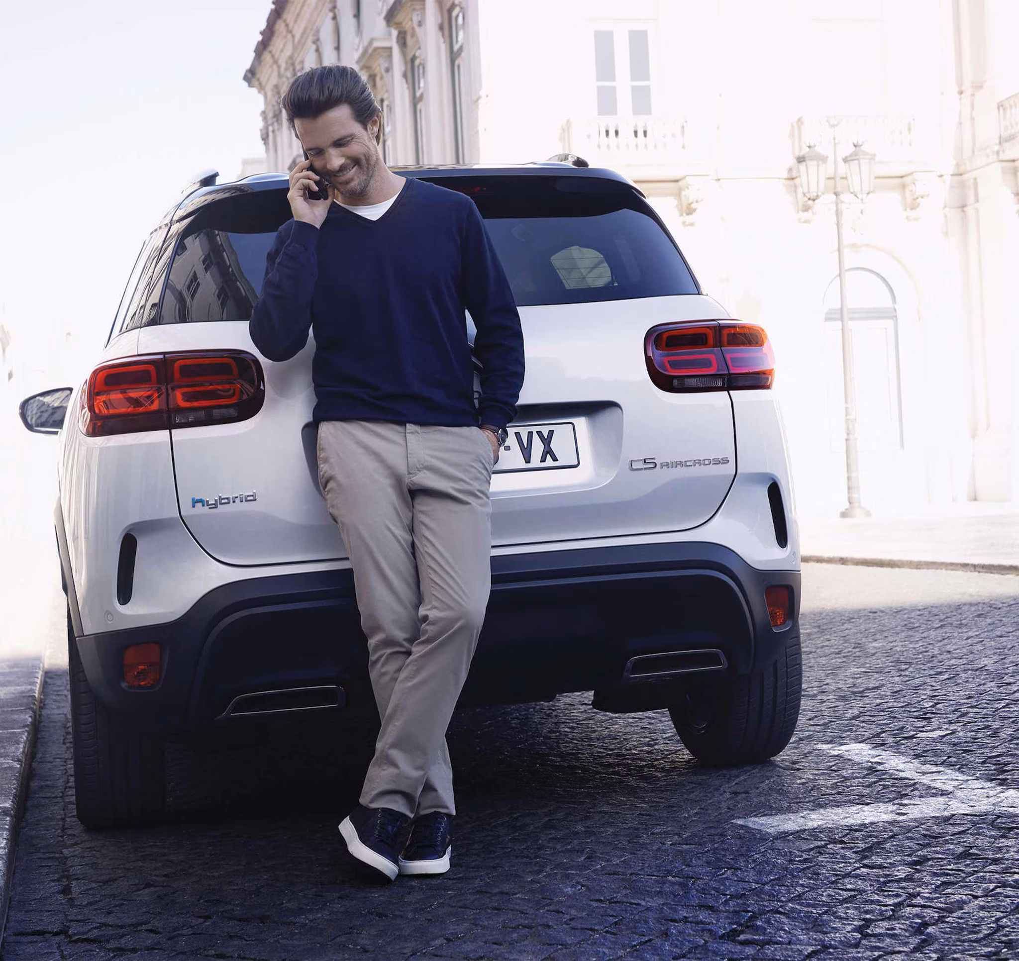 Mann lehnt entspannt am Citroën C5 Aircross Hybrid und telefoniert in der Stadt
